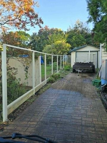The scene shows a mid grey corrugated steel fence where residential buildings appear beyond the line.