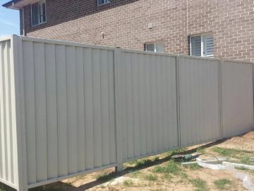 Cream Colorbond privacy fence standing beside a brick house on a bare yard