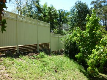 Pale Colorbond privacy fence with a lattice topper and bamboo edging in a garden