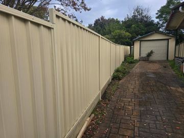Cream Colorbond privacy fence running beside a paved driveway to a garage