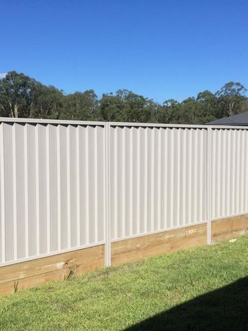 Long white Colorbond privacy fence standing on a timber plinth across a lawn