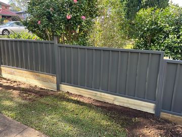 Charcoal Colorbond privacy fence sitting on a new timber sleeper retaining wall beside garden shrubs