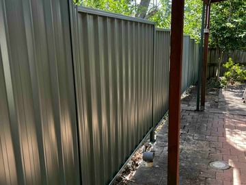 Charcoal Colorbond privacy fence hard against a narrow paved path