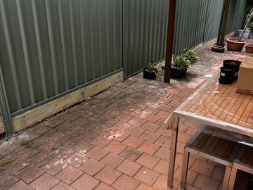 Light grey Colorbond privacy fence along a paved courtyard with a table and pot plants