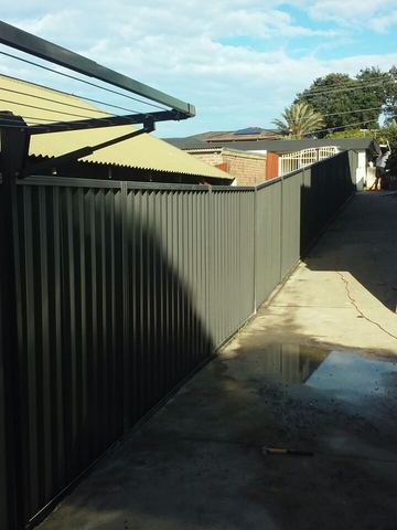 Dark Colorbond privacy fence running the length of a wet concrete yard