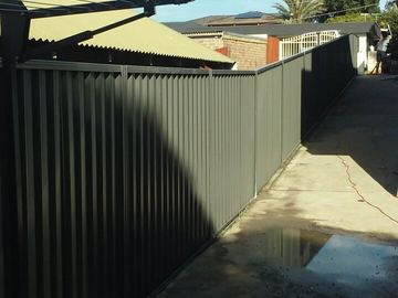 Dark Colorbond privacy fence running the length of a wet concrete yard