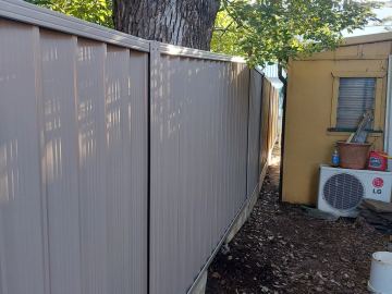 Beige Colorbond privacy fence turning a corner beside a cream garden shed