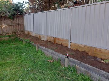 Cream Colorbond privacy fence standing on a raised timber sleeper garden bed