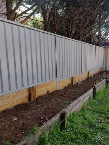 Cream Colorbond privacy fence with a newly filled timber garden bed at the base