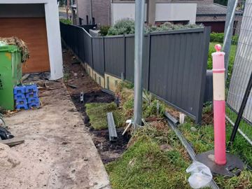 Charcoal Colorbond privacy fence on a pale plinth running beside a new house driveway