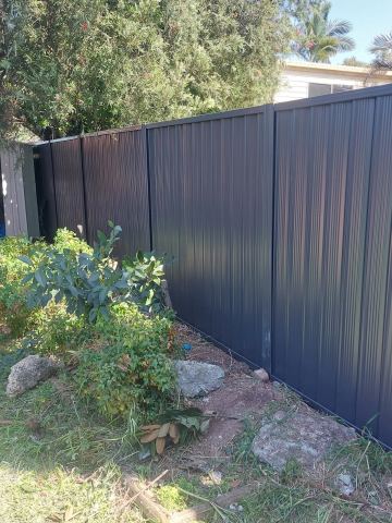 Close view of charcoal Colorbond privacy sheets with garden growth at the base