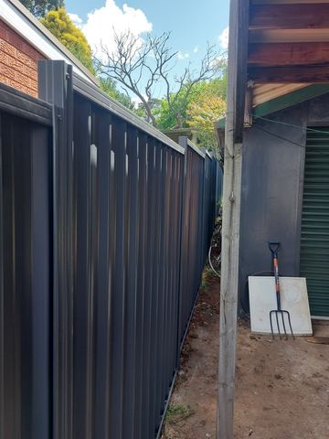 Charcoal Colorbond privacy fence running toward a matching roller door