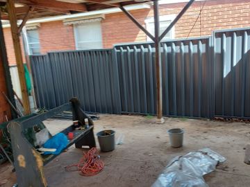 Charcoal Colorbond privacy fence across an open backyard with buckets on the dirt