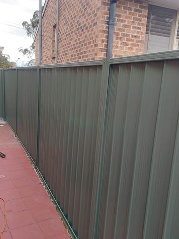 Charcoal Colorbond privacy fence following a red paved path