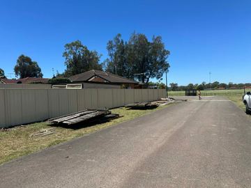 Cream Colorbond privacy fence along a sealed road with leftover boards on the grass