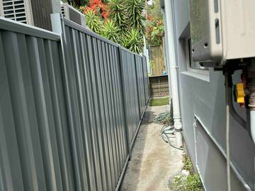 Mid grey Colorbond privacy fence forming a narrow side passage beside a house wall