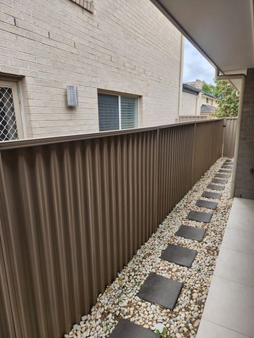 Looking along a cream Colorbond privacy fence beside a pebble path and house windows