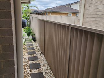 Cream Colorbond privacy fence running under the eave beside a pebble-lined path
