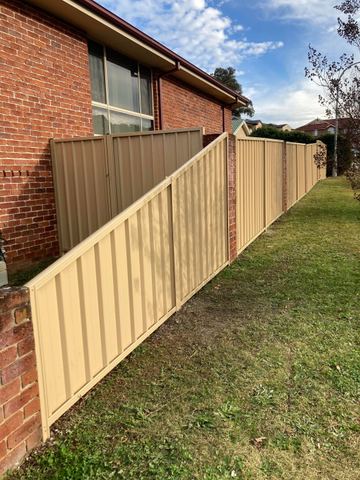 Long cream Colorbond privacy fence along a side lawn beside a brick house