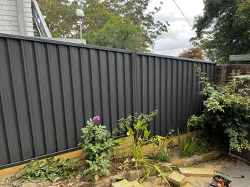 Charcoal Colorbond privacy fence running through a planted garden bed