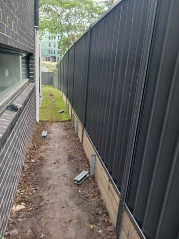 Charcoal Colorbond privacy fence along a dirt side yard beside a house wall