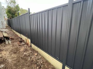 Long charcoal Colorbond privacy fence on a cleared dirt boundary
