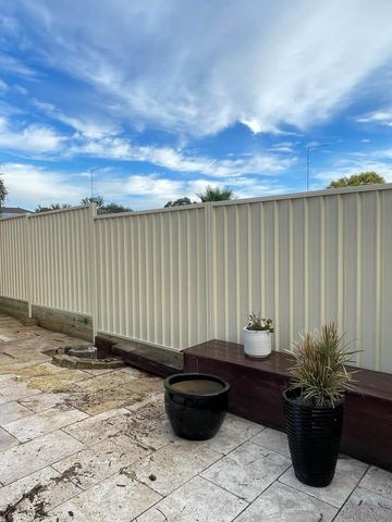 Cream Colorbond privacy fence on a paved courtyard with a bench and planter