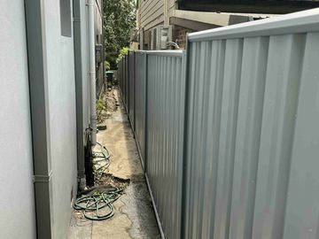 Light grey Colorbond privacy fence closing a narrow service passage beside a house