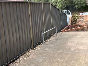 Charcoal Colorbond privacy fence beside a concrete pad and gravel garden