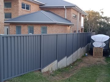 Charcoal Colorbond privacy fence across the front of a house with a covered barbecue