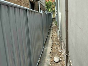 Mid grey Colorbond privacy fence forming a tight side path against a house wall