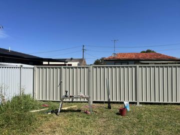 Cream Colorbond privacy fence across a lawn with leftover rails on the grass