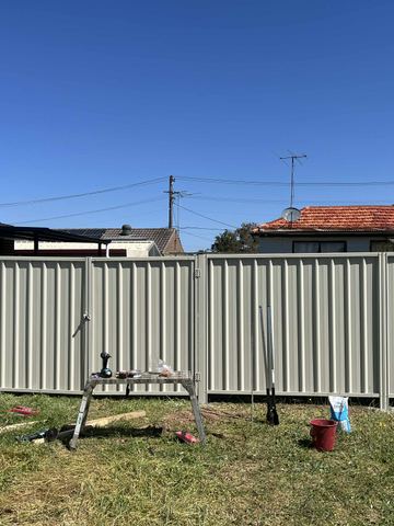 Cream Colorbond privacy fence across a lawn with leftover rails on the grass