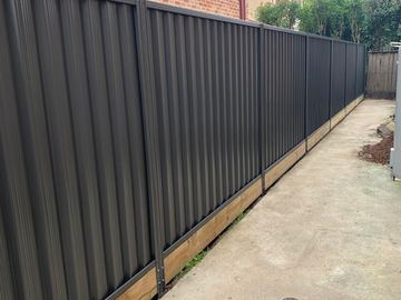 Long charcoal Colorbond privacy fence on a timber sleeper wall beside a concrete path
