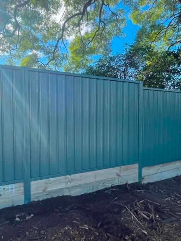Pale Colorbond privacy fence on a new timber sleeper wall with a ladder beside it
