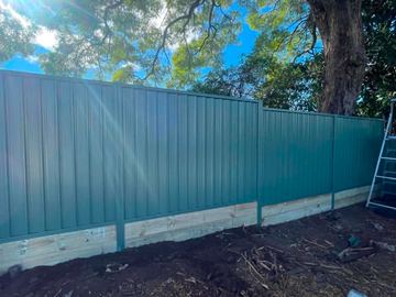 Pale Colorbond privacy fence on a new timber sleeper wall with a ladder beside it