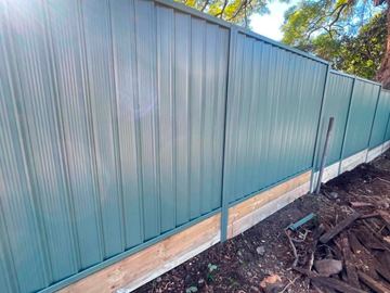 Teal Colorbond privacy fence along a cleared dirt yard