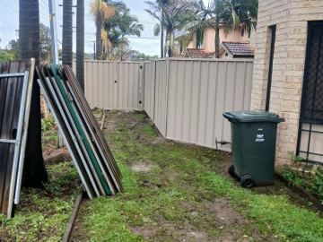Cream Colorbond privacy fence turning a corner across a grassed backyard