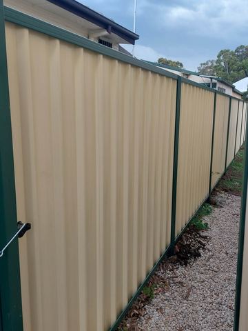 Cream Colorbond privacy fence with a drop bolt on the near post beside a gravel edge