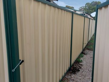 Cream Colorbond privacy fence with a drop bolt on the near post beside a gravel edge
