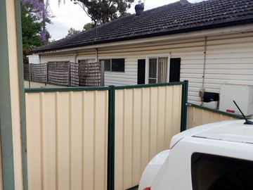 Cream Colorbond privacy fence with green posts behind a weatherboard house