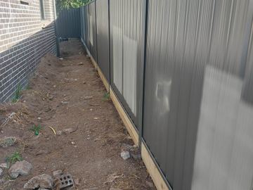Charcoal Colorbond privacy fence on a pale sleeper along a dirt side yard