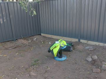 Charcoal Colorbond privacy fence turning a corner with a high-vis vest on the dirt