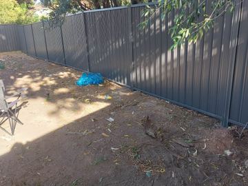 Charcoal Colorbond privacy fence across a dirt backyard with a blue bag on the ground