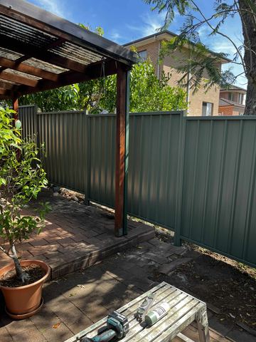 Green Colorbond privacy fence beside a timber pergola post on paving