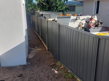 Charcoal Colorbond privacy fence running past a garden shed with tools on top