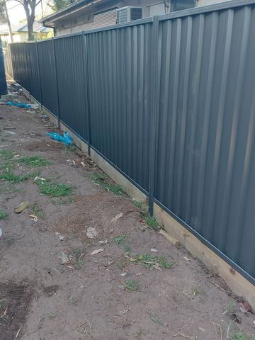 Charcoal Colorbond privacy fence on a dirt backyard line with a pale sleeper