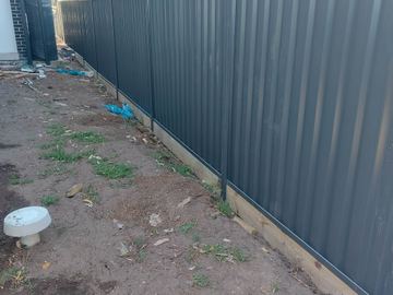 Charcoal Colorbond privacy fence on a dirt backyard line with a pale sleeper