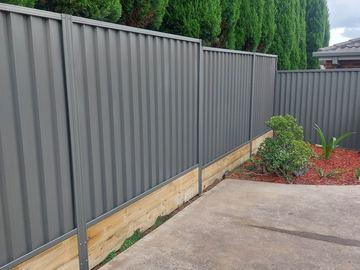 Charcoal Colorbond privacy fence on a timber sleeper beside a concrete pad and garden bed