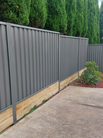 Charcoal Colorbond privacy fence on a timber sleeper beside a concrete pad and garden bed